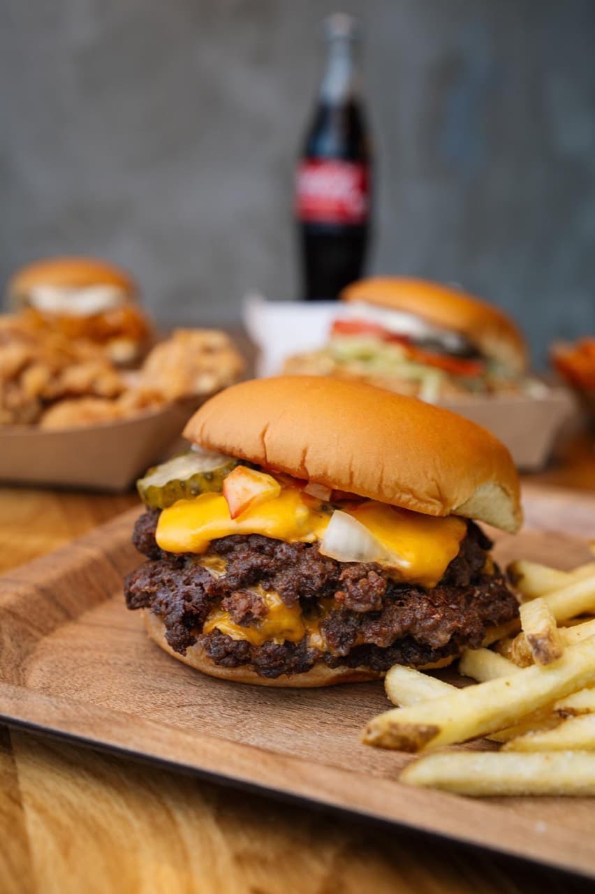 BUNEX Smashburger mit Pommes und weiteren Gerichten im Hintergrund